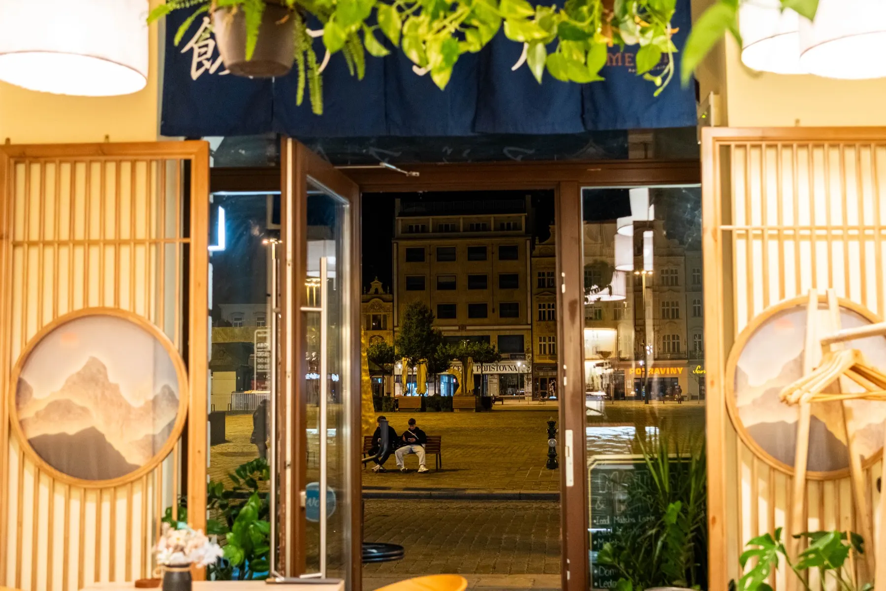 Vchod do restaurace s noren závěsem a výhledem na náměstí
